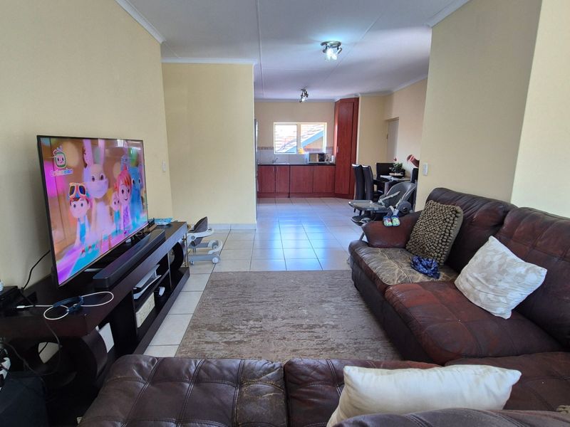 An open-plan living and kitchen area featuring tiled flooring and built-in kitchen cabinetry, providing a functional and connected living space.