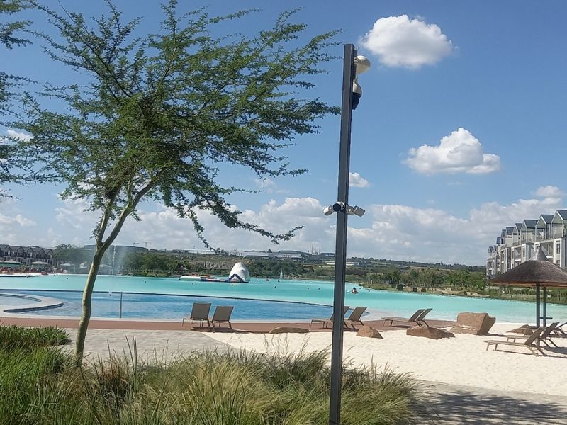 A well-maintained communal pool area featuring a sandy beach, paved walkways, and landscaped surroundings within a modern apartment complex.