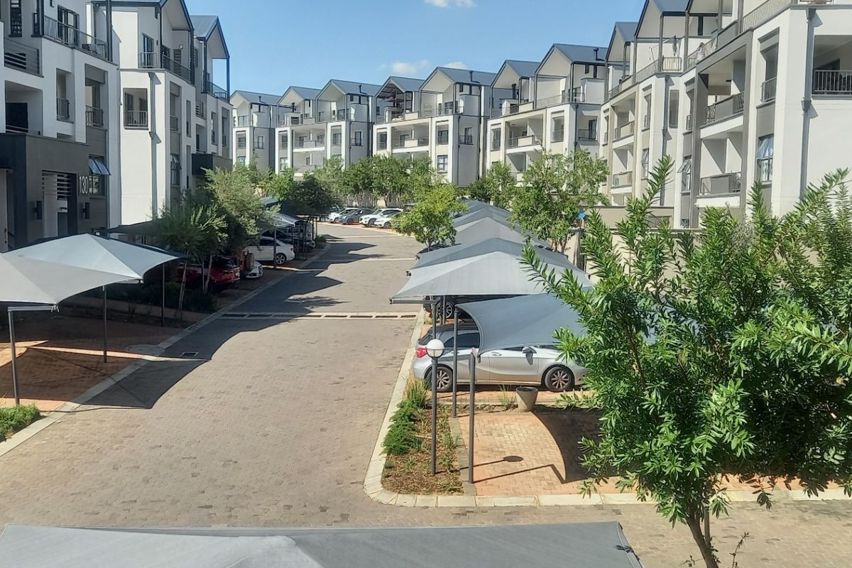View of the apartment complex grounds featuring paved driveways, covered parking bays, and established landscaped garden areas between the residential buildings.