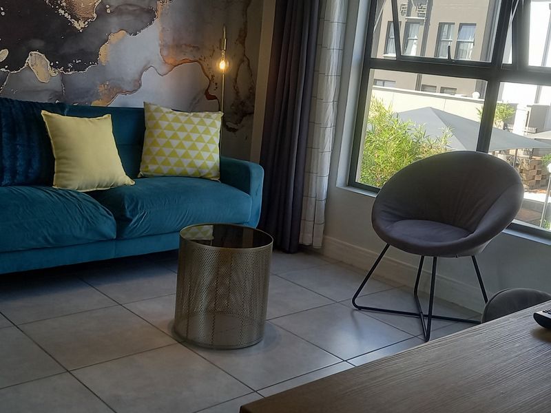 A well-lit living area featuring tiled flooring and a large window with views of the surrounding apartment complex.