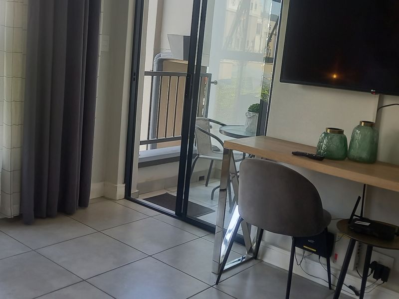 A modern living area featuring tiled flooring, a built-in desk, and a sliding glass door providing access to a private balcony.