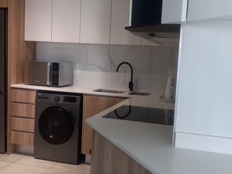 Modern kitchen featuring sleek white and wood-grain cabinetry, stone countertops, marble-look splashback, and integrated appliances including an induction hob and extractor fan.
