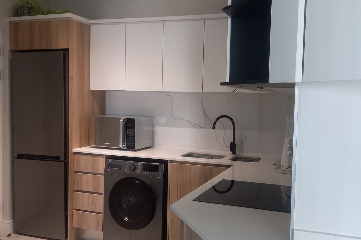 Modern kitchen featuring sleek white and wood-grain cabinetry, stone countertops, marble-look splashback, and integrated appliances including a hob and microwave.