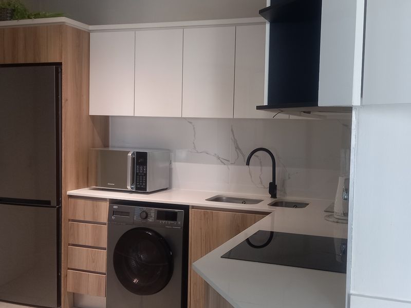 Modern kitchen featuring sleek white and wood-grain cabinetry, stone countertops, marble-look splashback, and integrated appliances including a hob and microwave.