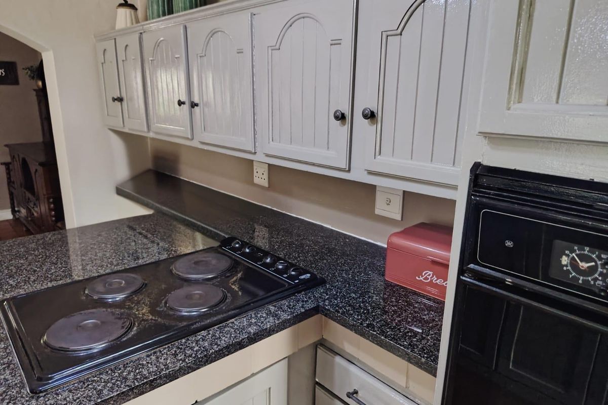 A functional kitchen featuring granite countertops, a built-in electric hob, and painted cabinetry with classic arched detailing.