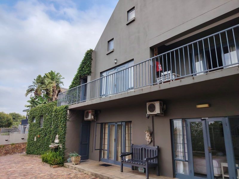 Rear elevation of a multi-story house featuring a balcony with metal railings, multiple sets of french doors, and paved outdoor area.