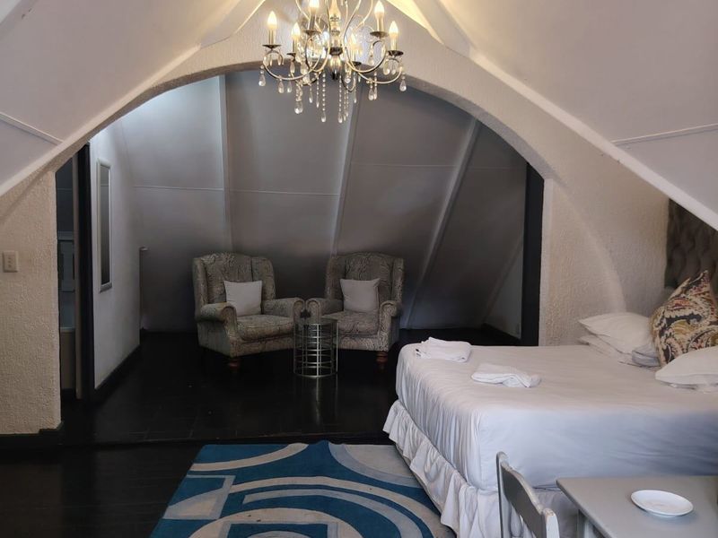 Spacious bedroom featuring a unique vaulted ceiling with an arched architectural detail, a central chandelier, and dark timber flooring.