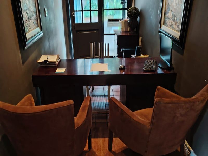 A compact office space featuring dark walls, tiled flooring, and a glass-panelled exterior door, suitable for a private workspace or reception area.