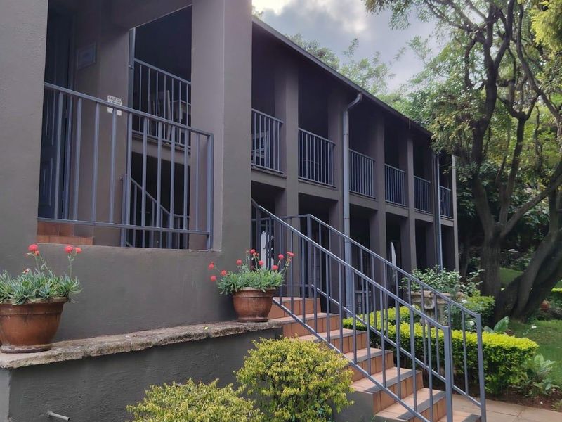 A multi-level rear exterior view featuring a covered balcony, metal railings, tiled staircase, and a stone water feature set within a landscaped garden.