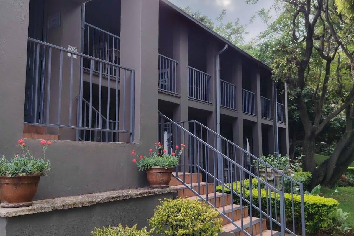 A multi-level rear exterior view featuring a covered balcony, metal railings, tiled staircase, and a stone water feature set within a landscaped garden.