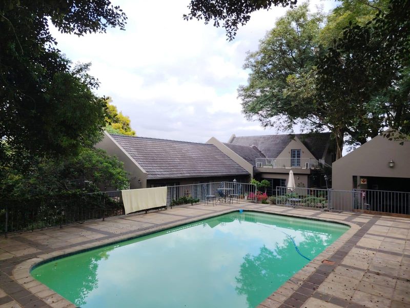 A rear exterior view featuring a swimming pool with tiled surround, metal fencing, and a multi-level house structure with a pitched tiled roof.