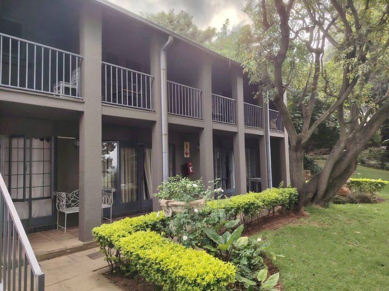 A two-story rear elevation featuring covered balconies with metal railings, sliding glass doors, and a paved patio area overlooking a landscaped garden.