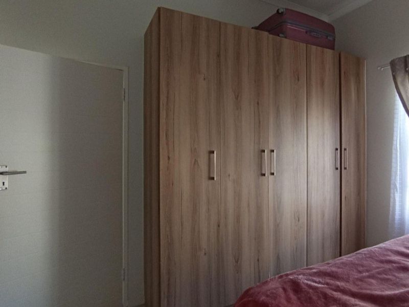 A bedroom featuring a modern wood-finish built-in wardrobe with sleek metal handles.
