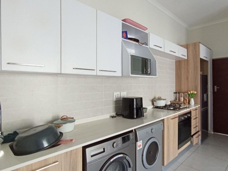 Modern kitchen featuring sleek white and wood-grain cabinetry, stone countertops, integrated appliances, and a tiled backsplash in a clean, functional layout.
