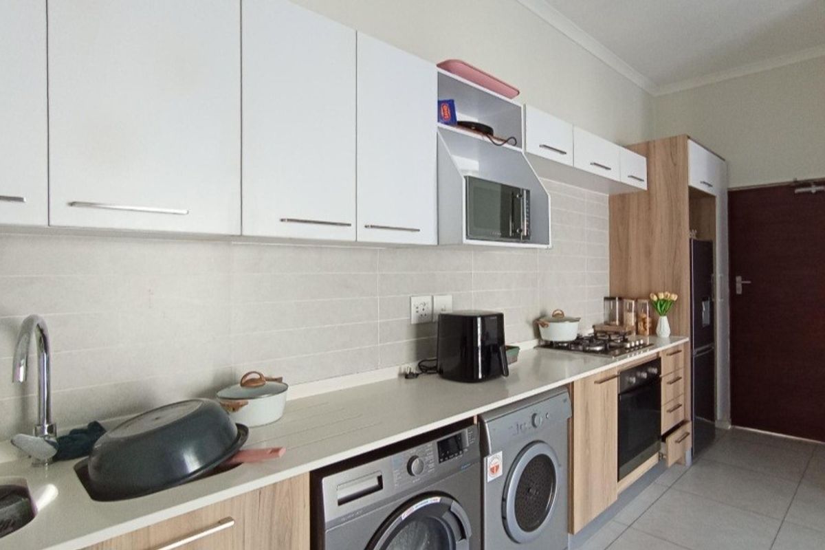 Modern kitchen featuring sleek white and wood-grain cabinetry, stone countertops, integrated appliances, and a tiled backsplash in a clean, functional layout.