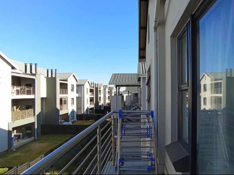 A spacious apartment balcony featuring a stainless steel balustrade and views over the surrounding residential complex.