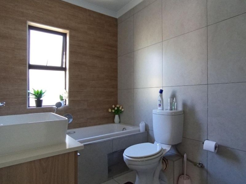 Modern bathroom featuring a built-in bathtub, vessel sink vanity, and neutral wall tiling with a window for natural light.