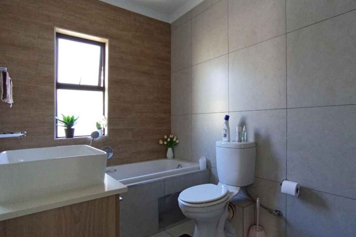 Modern bathroom featuring a built-in bathtub, vessel sink vanity, and neutral wall tiling with a window for natural light.