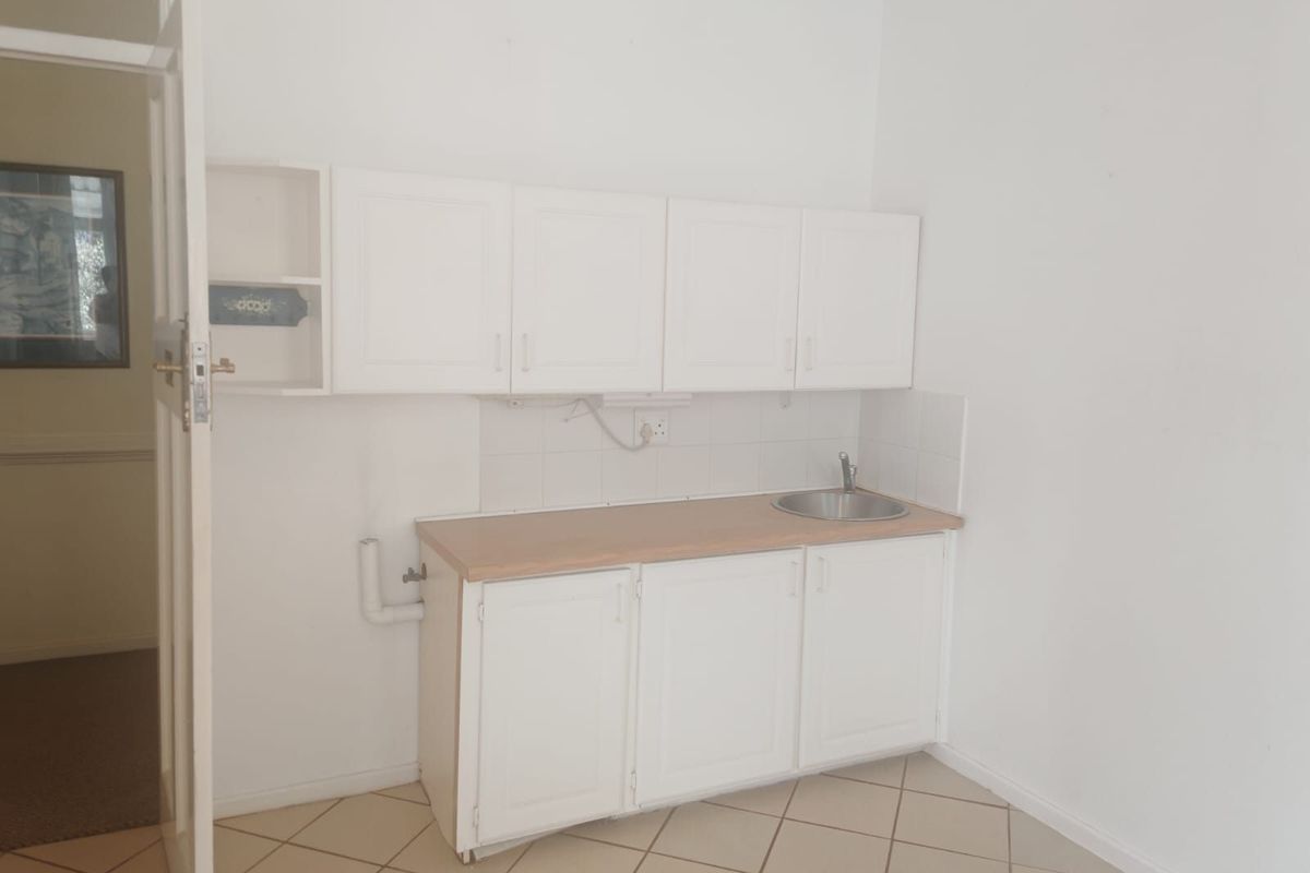 A compact kitchen area featuring white built-in cabinetry, a laminate countertop with an integrated sink, and tiled flooring.