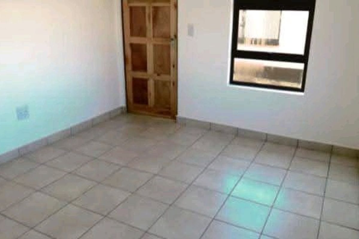 An empty bedroom featuring neutral tiled flooring, a timber door, and an aluminium-framed window, providing a clean and versatile space.