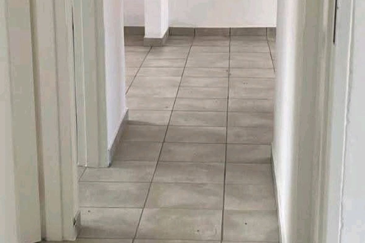 A vacant hallway featuring neutral ceramic floor tiles and white painted walls, providing a clean and simple transition space within the townhouse.