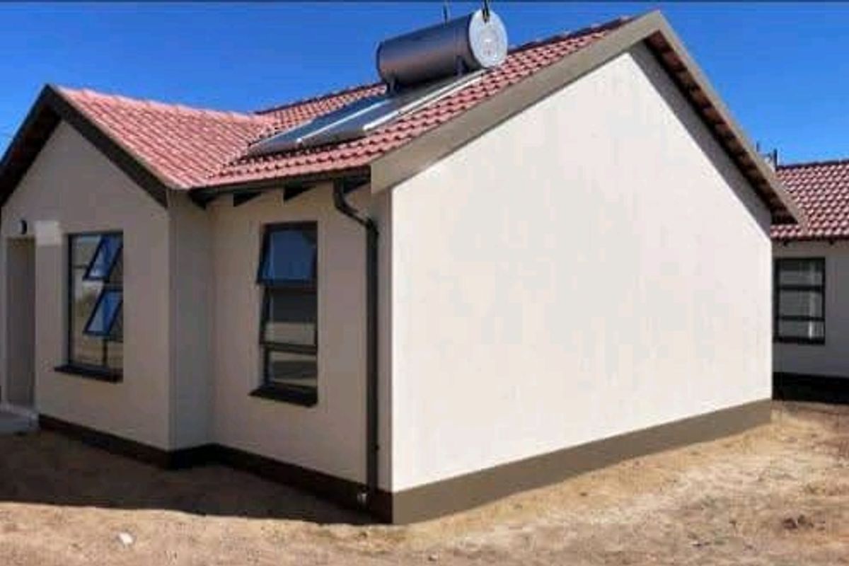 A modern townhouse exterior featuring a tiled roof, solar water heating system, and clean plastered walls with aluminium window frames.