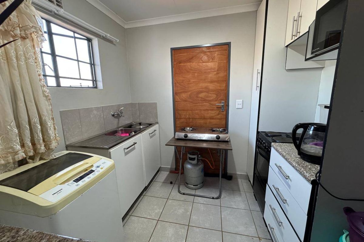 Compact kitchen featuring tiled flooring, built-in cabinetry, laminate countertops, a stainless steel sink, and integrated oven with extractor fan.
