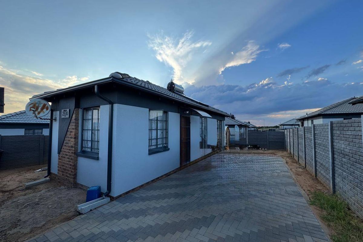 Rear view of the property featuring a paved driveway, precast boundary wall, and installed solar water heating system on the roof.