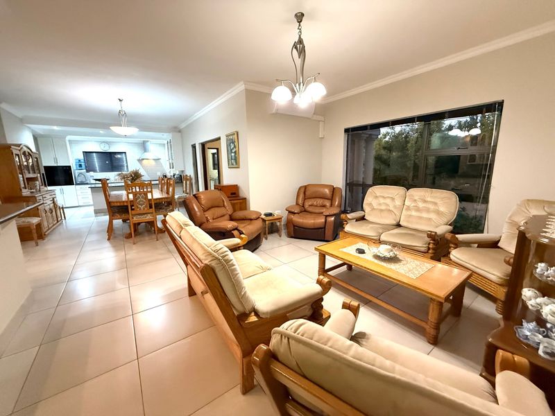Spacious open-plan living and dining area featuring tiled flooring, cove cornicing, and a functional kitchen with built-in cabinetry and appliances.