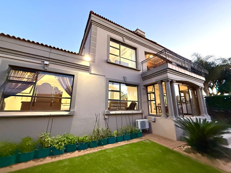 Rear elevation of a two-story townhouse featuring a manicured lawn, upper-level balcony with wrought iron railing, and large windows providing natural light.