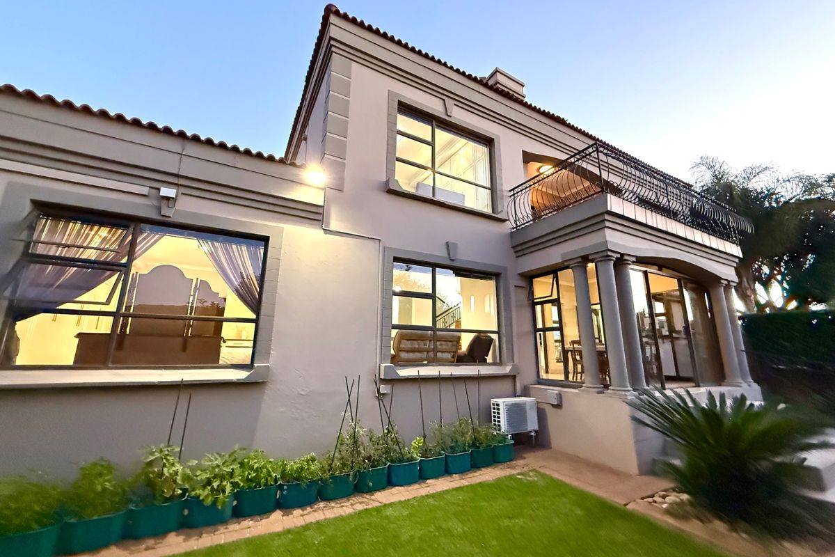 Rear elevation of a two-story townhouse featuring a manicured lawn, upper-level balcony with wrought iron railing, and large windows providing natural light.