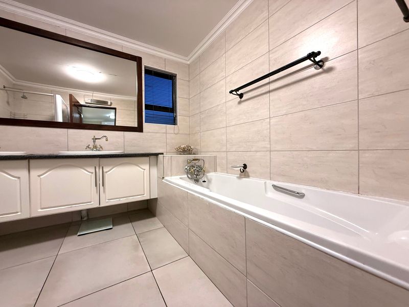 A clean, well-maintained bathroom featuring a built-in vanity, large mirror, and a tiled bathtub area with modern fixtures.