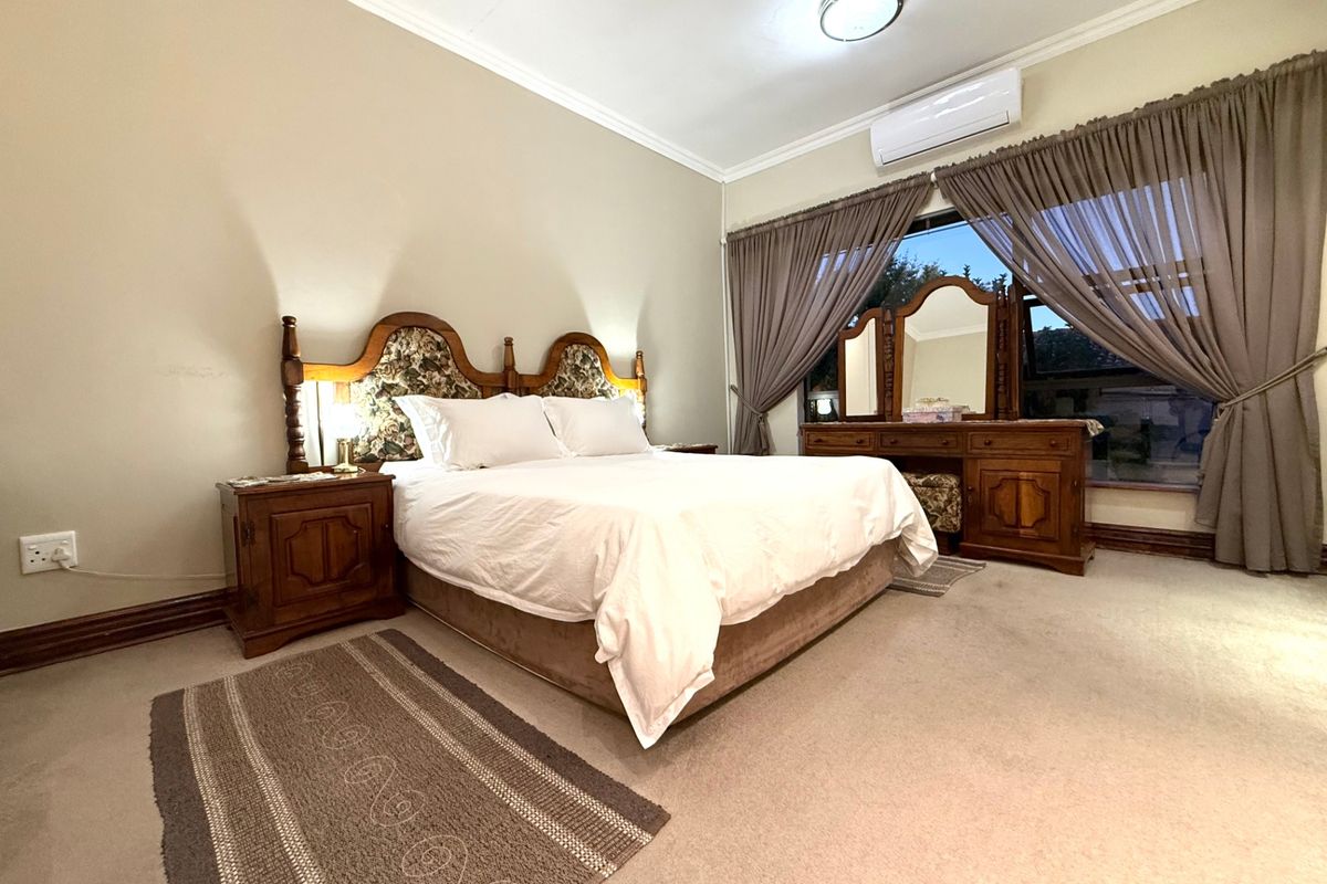 A spacious bedroom featuring neutral wall tones, carpeted flooring, and a wall-mounted air conditioning unit, providing a comfortable and functional living space.