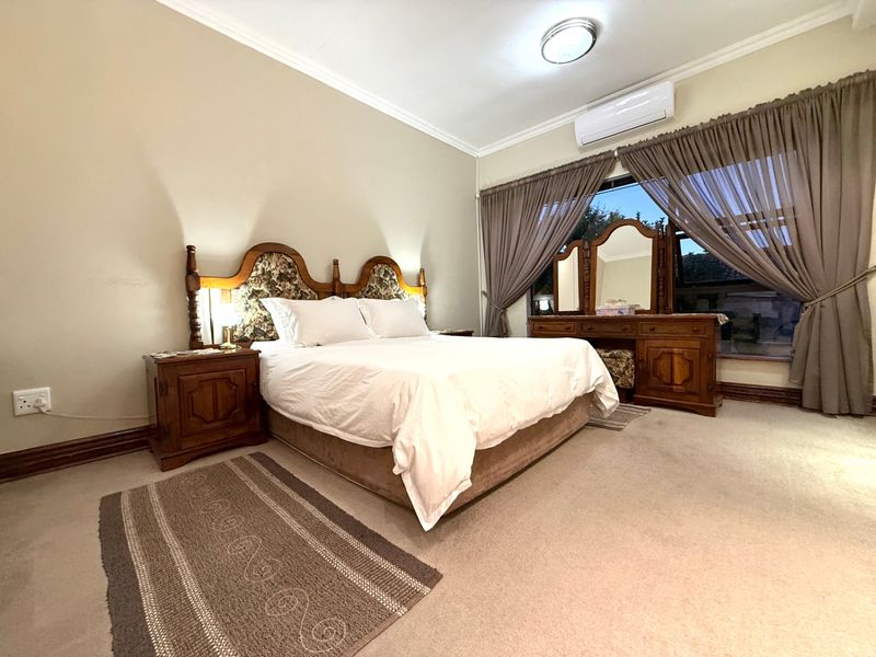 A spacious bedroom featuring neutral wall tones, carpeted flooring, and a wall-mounted air conditioning unit, providing a comfortable and functional living space.