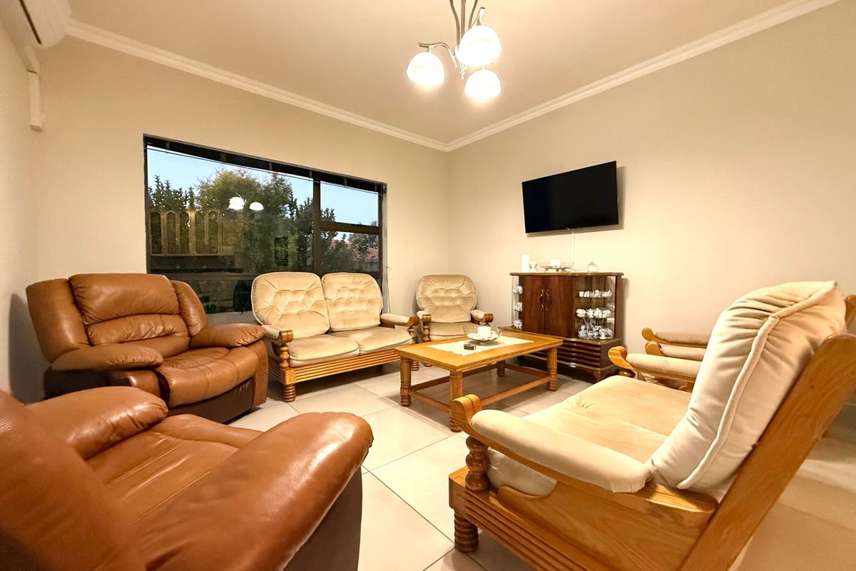 A well-maintained living room featuring neutral tiled flooring, coving, and a split-system air conditioner, offering a comfortable and functional space.