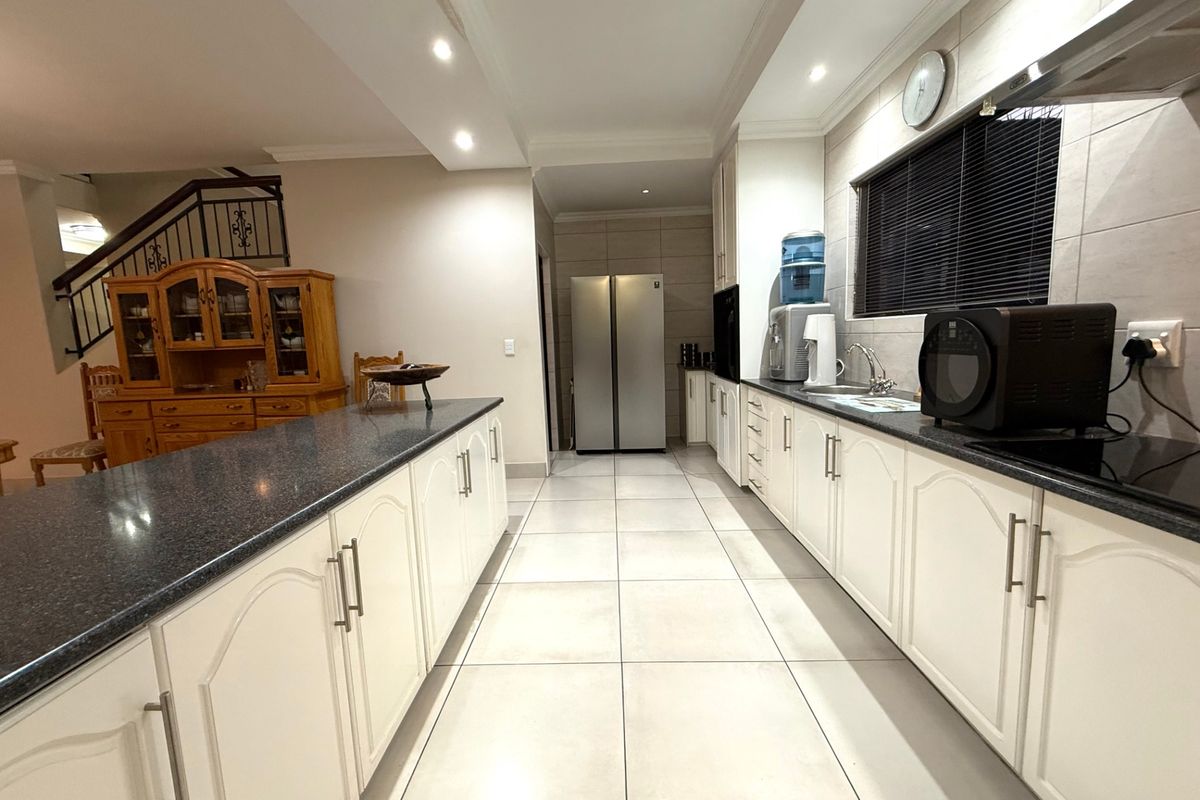 Spacious kitchen featuring white cabinetry, granite countertops, tiled flooring, and recessed lighting, seamlessly flowing into the adjacent living area with staircase access.