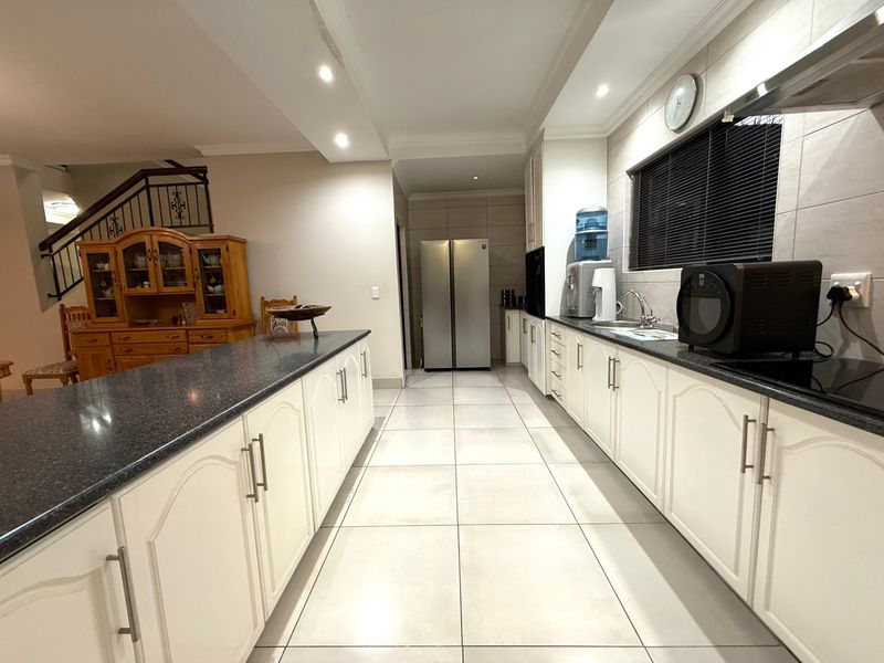 Spacious kitchen featuring white cabinetry, granite countertops, tiled flooring, and recessed lighting, seamlessly flowing into the adjacent living area with staircase access.