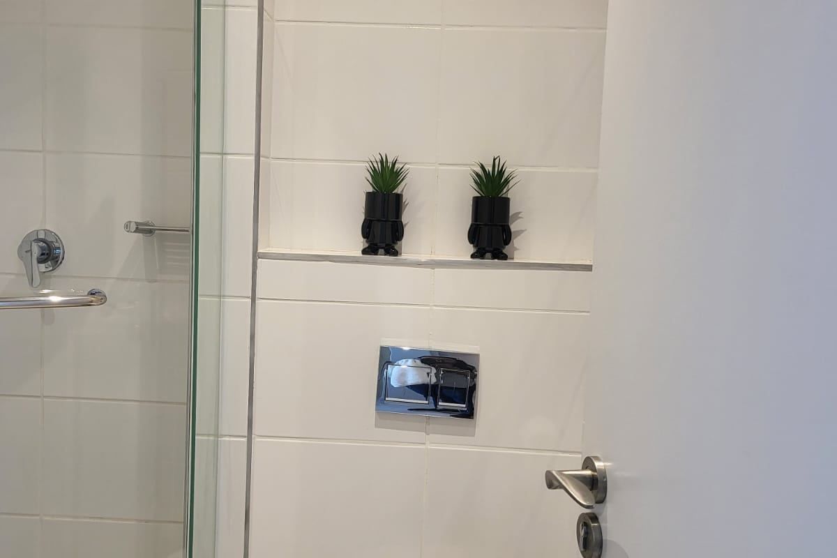 A modern bathroom featuring a glass-enclosed shower, wall-mounted toilet with a chrome flush plate, and white tiled walls.