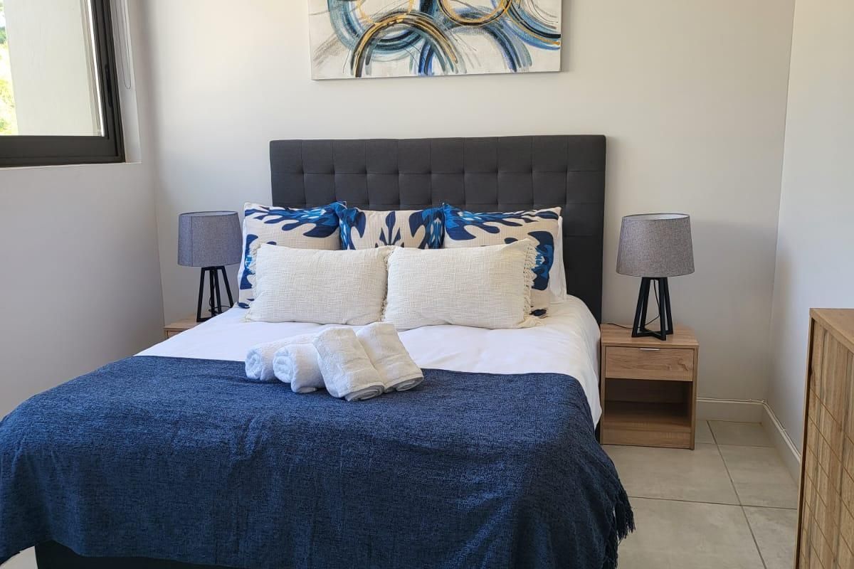 A well-maintained bedroom featuring neutral tiled flooring, recessed ceiling lighting, and a large window providing natural light.