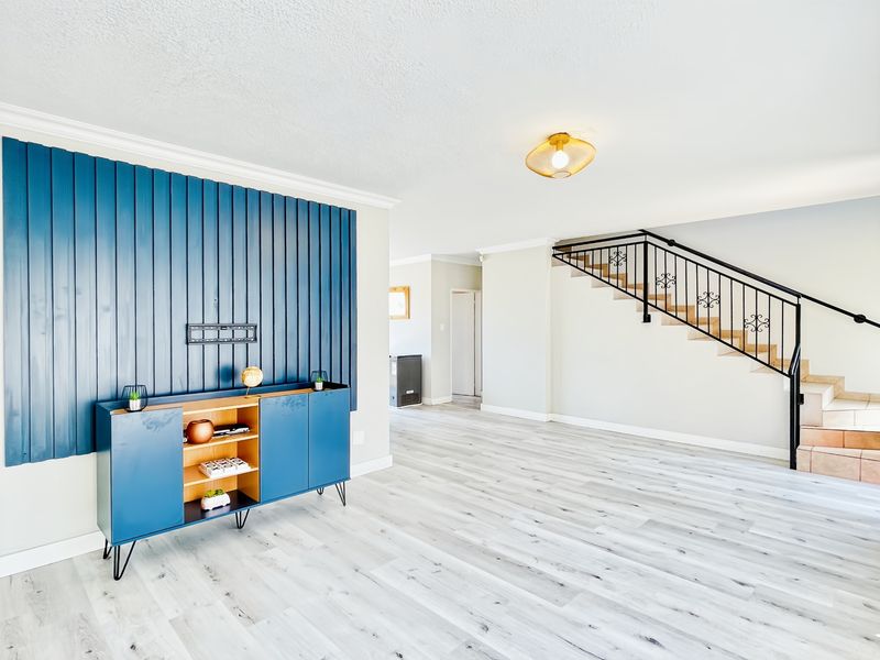 Spacious living area featuring modern laminate flooring, a striking blue decorative feature wall, and an elegant wrought iron staircase leading to the upper level.