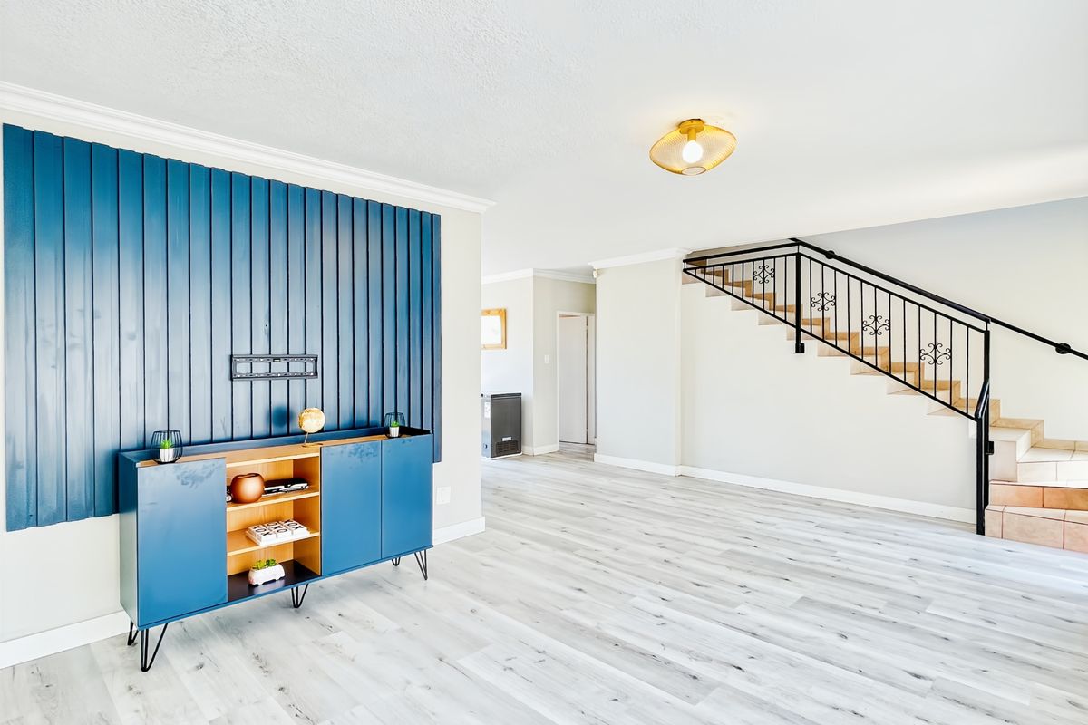 Spacious living area featuring modern laminate flooring, a striking blue decorative feature wall, and an elegant wrought iron staircase leading to the upper level.