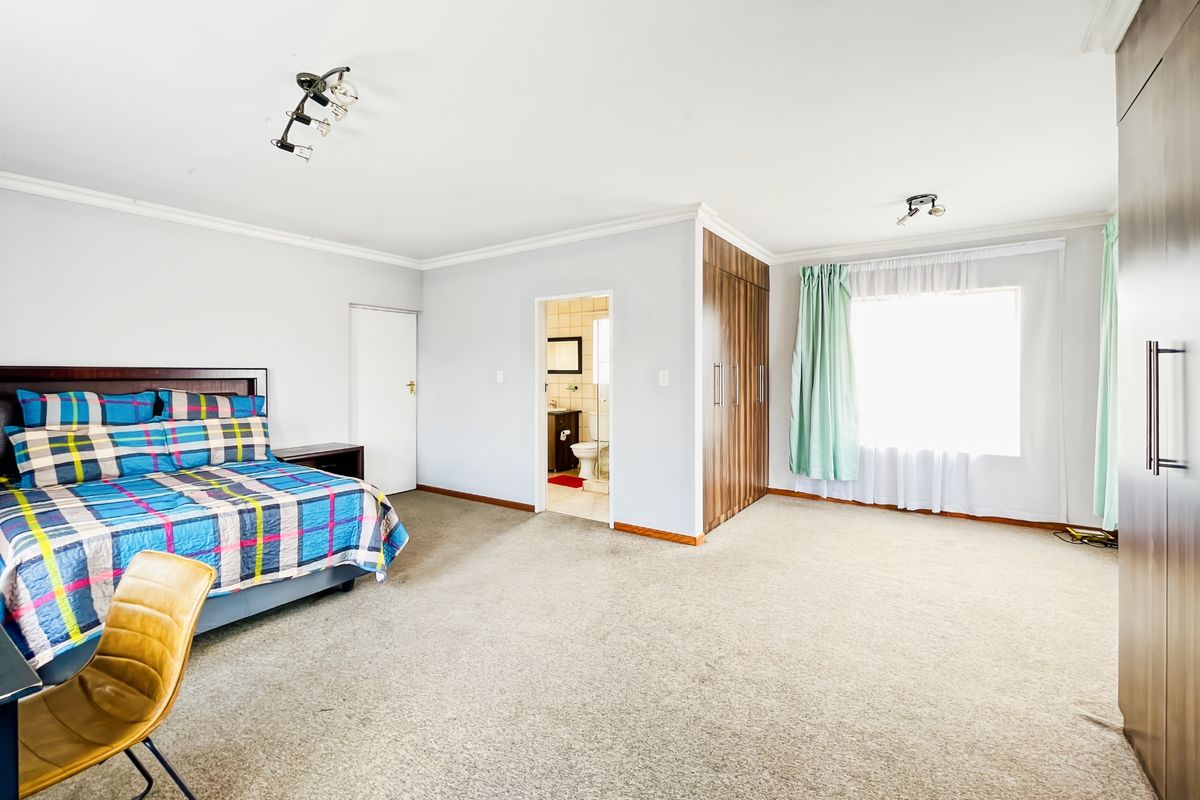 Spacious bedroom featuring neutral walls, carpeted flooring, built-in wooden cupboards, and an adjoining en-suite bathroom with natural light.