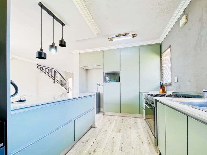 Modern kitchen featuring light green cabinetry, stone countertops, integrated appliances, gas hob, and stylish pendant lighting with wood-look laminate flooring.