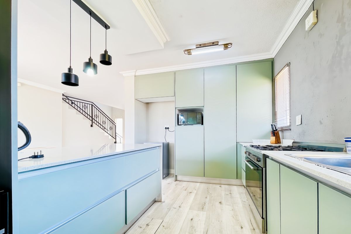 Modern kitchen featuring light green cabinetry, stone countertops, integrated appliances, gas hob, and stylish pendant lighting with wood-look laminate flooring.