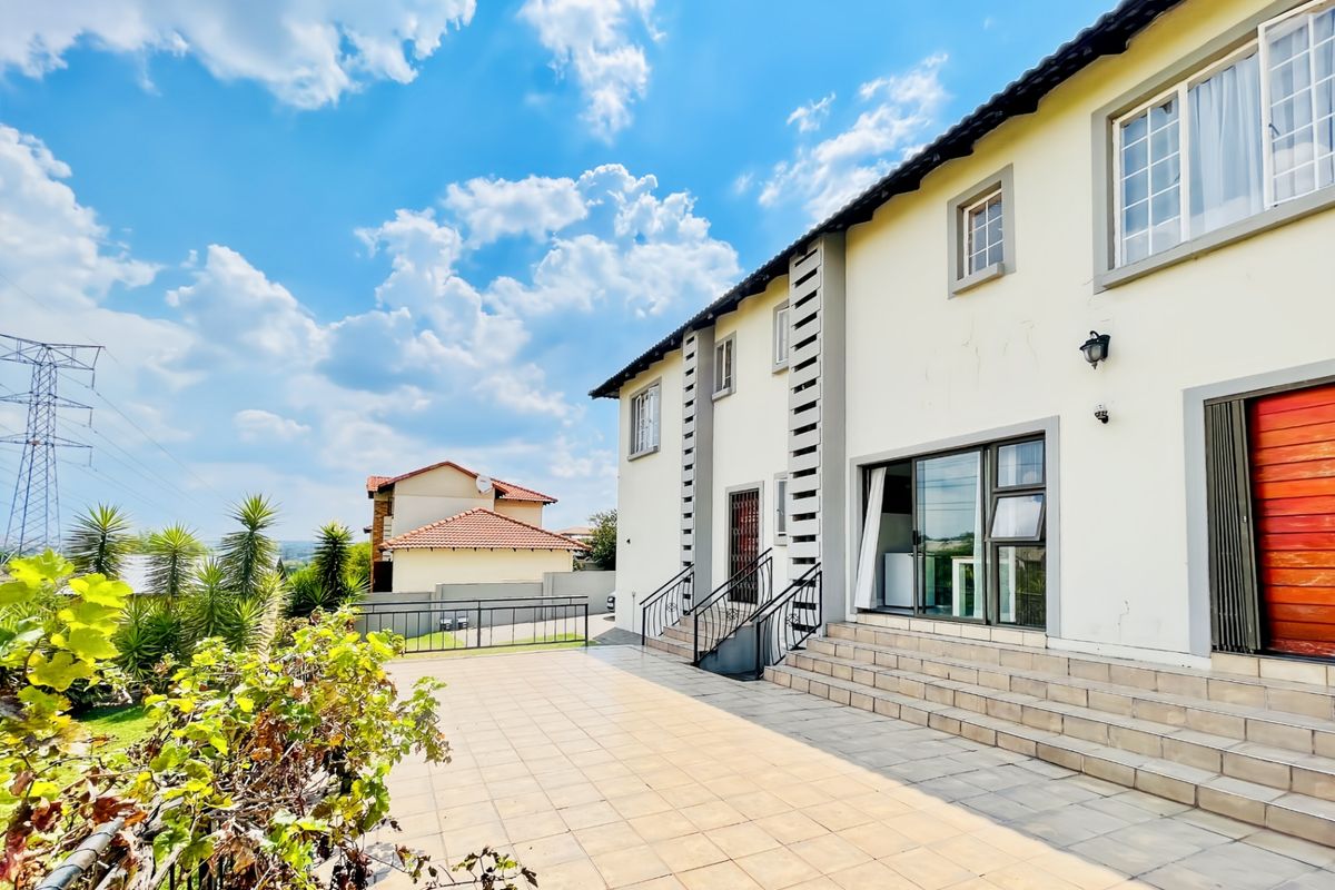 Rear view of the house featuring a spacious tiled patio, sliding glass doors, and stairs leading to the main living area.