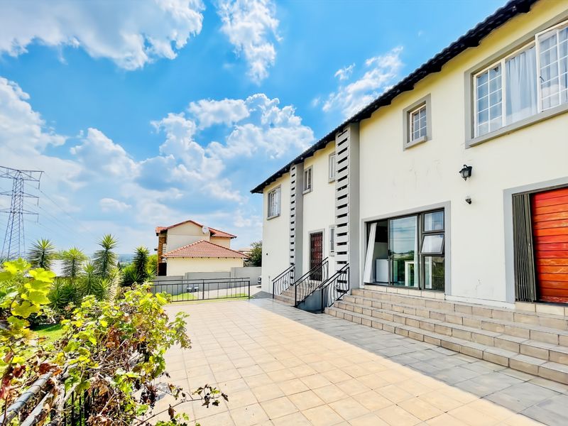 Rear view of the house featuring a spacious tiled patio, sliding glass doors, and stairs leading to the main living area.
