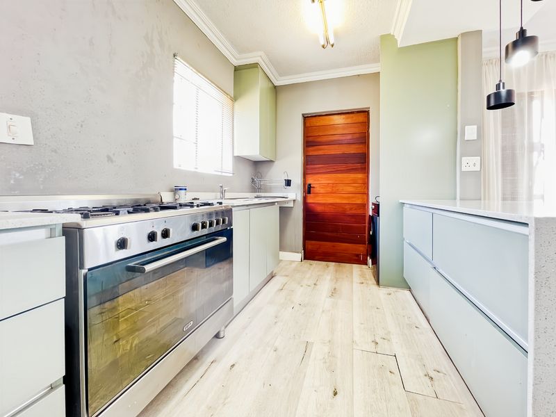 Modern kitchen featuring light-toned cabinetry, stone countertops, a stainless steel gas stove, and timber door access.
