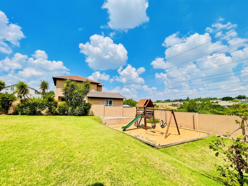 A spacious rear garden featuring a well-maintained lawn, perimeter walling, and a dedicated sand pit area with play equipment.
