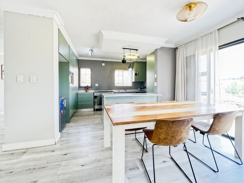 Modern open-plan kitchen and dining area featuring sleek green cabinetry, a central island, and direct access to the outdoors through sliding glass doors.