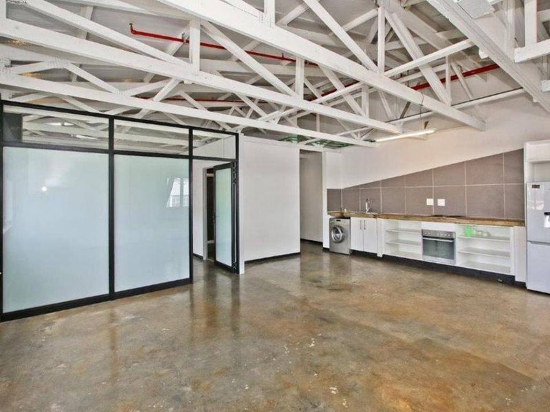 Open-plan living area featuring industrial-style exposed roof trusses, polished concrete floors, and a modern kitchen with built-in cabinetry and integrated appliances.